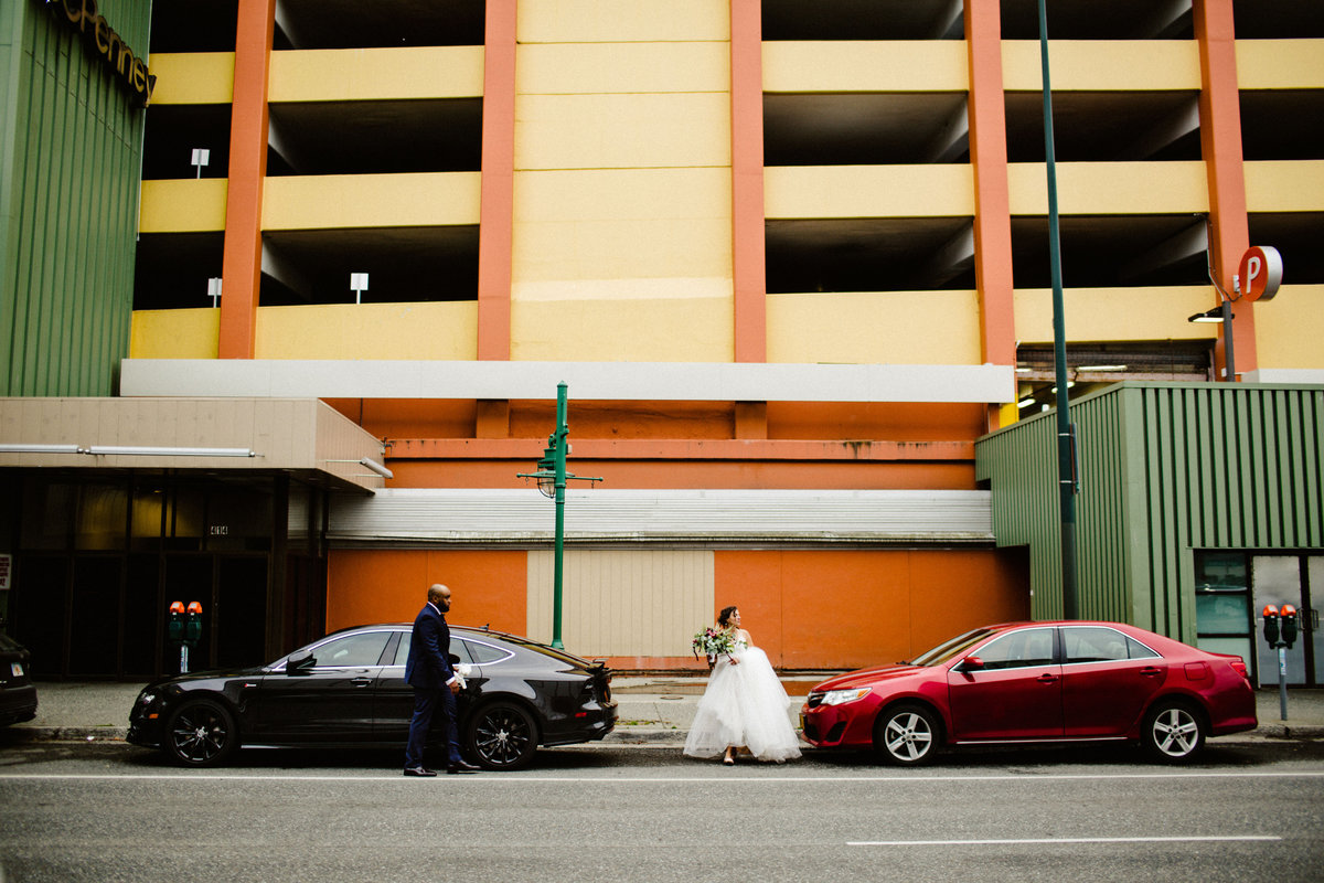 wedding couple crosses street in front of colorful parking garage in downtown anchorage