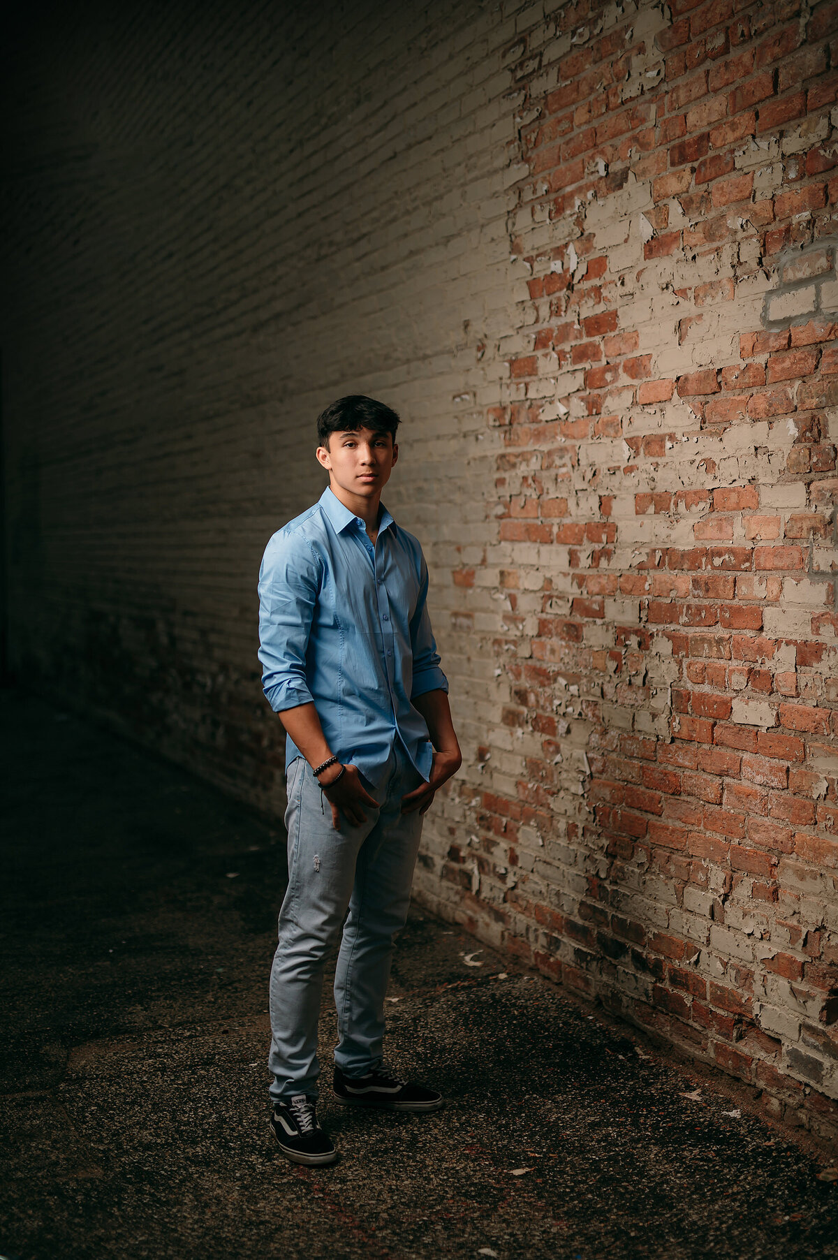 A young man from Waukesha West High School stands along a distressed brick wall in the Downtown area for his senior portraits.