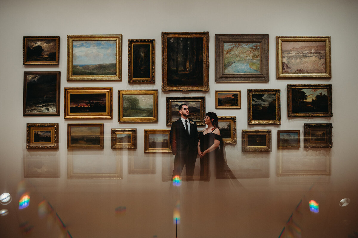 Newlyweds pose in front of wall art frmaes with a reflective bottom