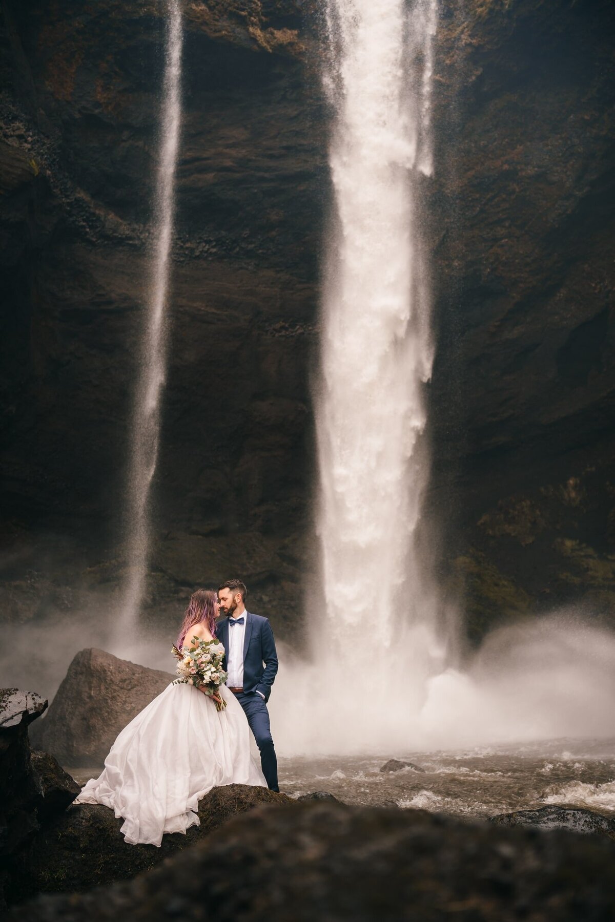 Hand in hand, this couple stands before the majestic Kvernufoss waterfalls in Iceland, creating a timeless portrait filled with love and the magic of nature.
