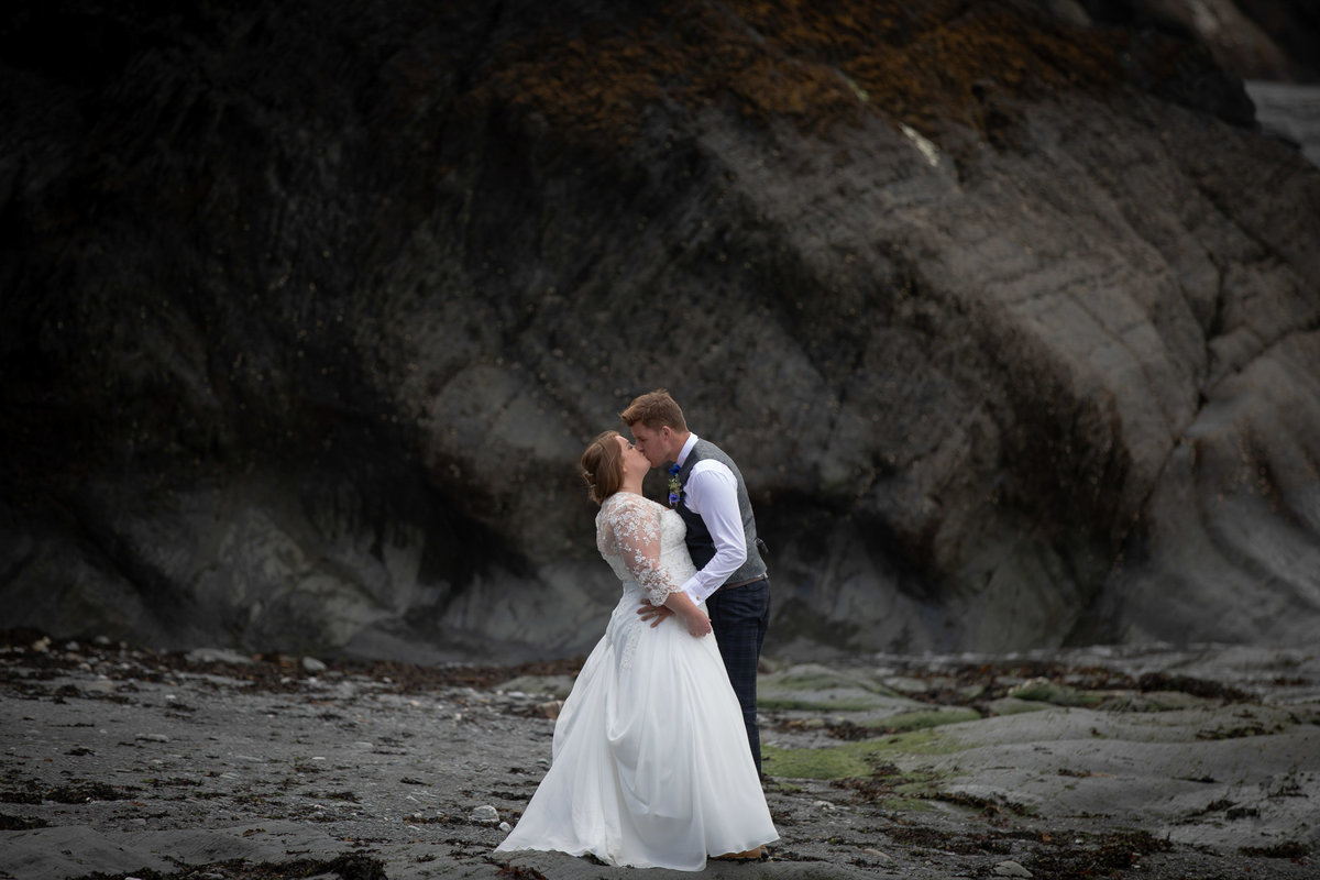 Kissing by the rocks at Tunnels Beaches wedding venue in Devon