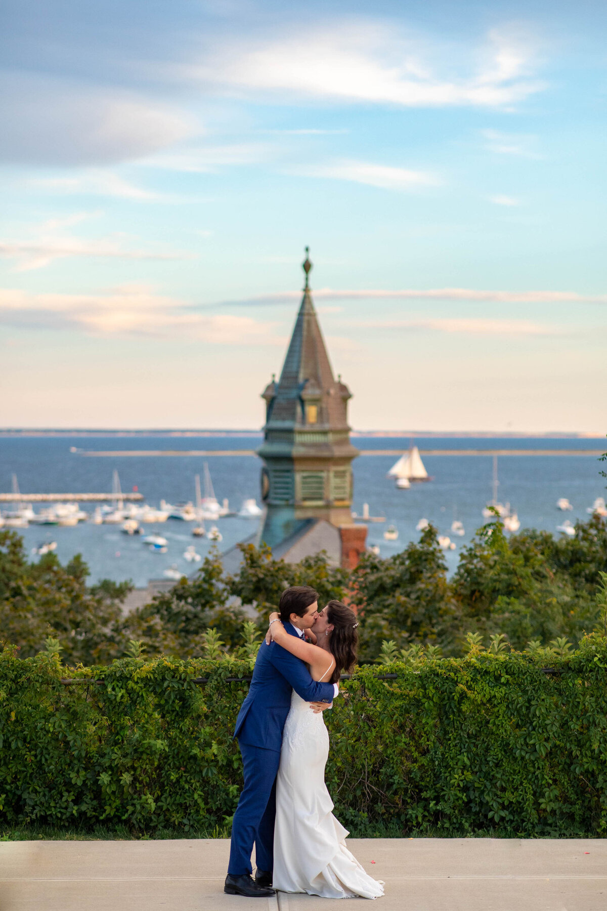 A couple kissing on an overlook looking out over boats on the water.