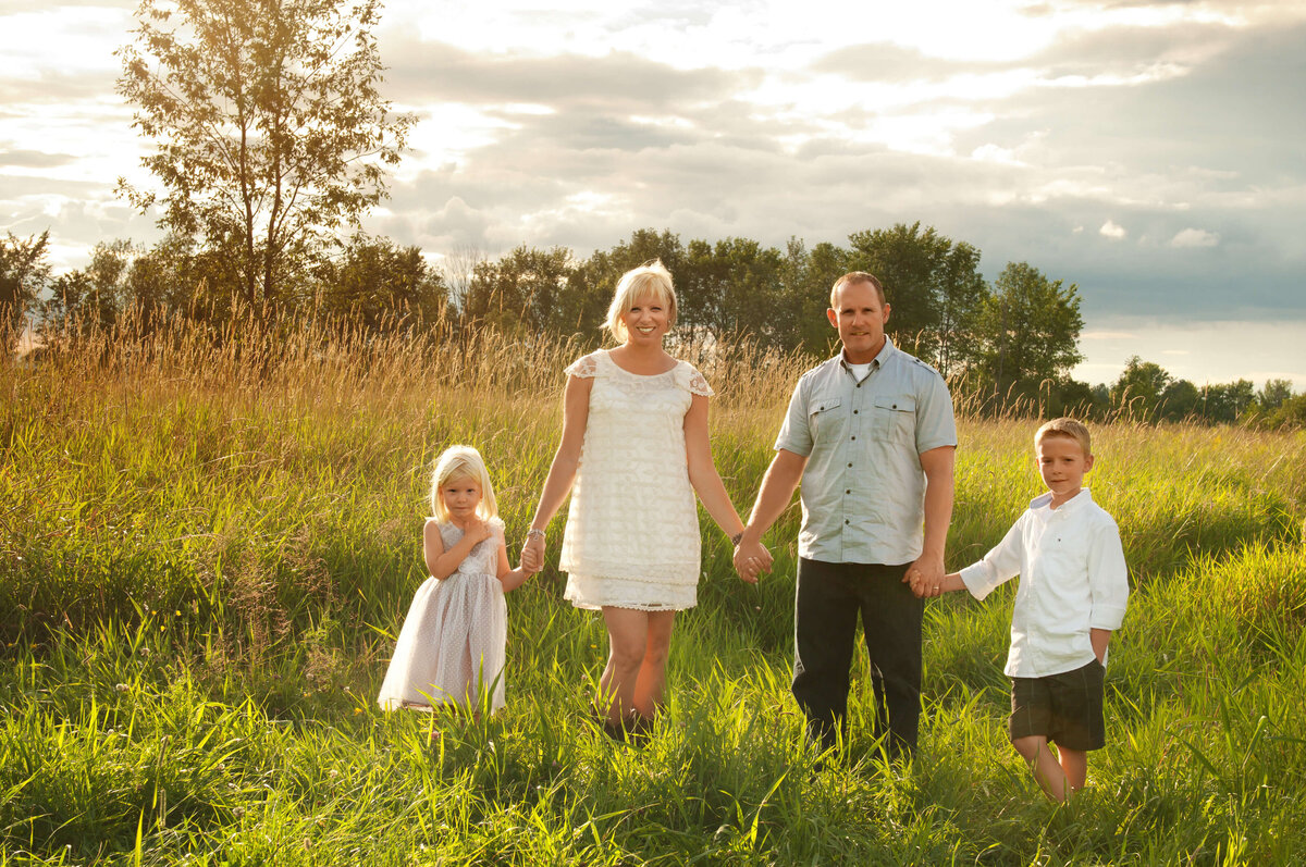 mom, dad and children holding hands in a field at sunset captured by Ottawa Family Photographer JEMMAN Photography