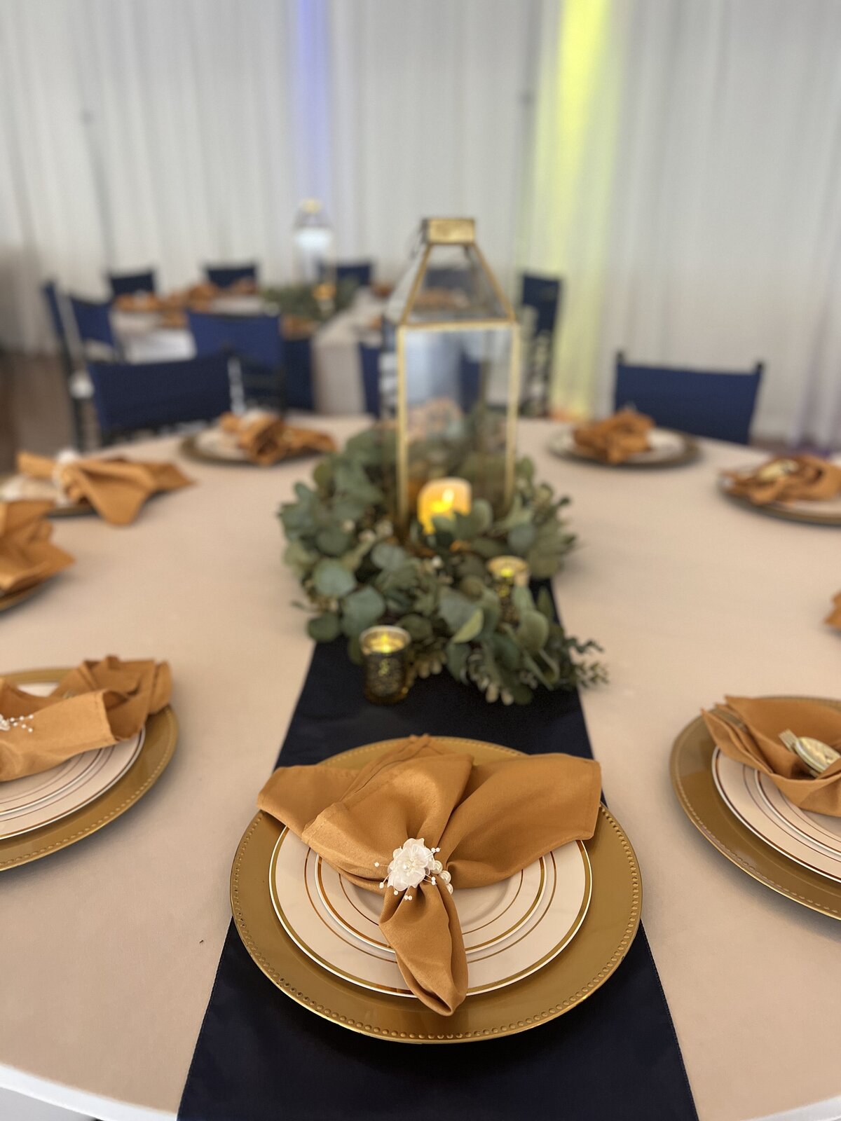 Birthday party guest table in our indoor banquet hall, The District, featuring our affordable classic decor package - Gold napkins, blue satin runners, and stunning gold lanterns create an elegant ambiance