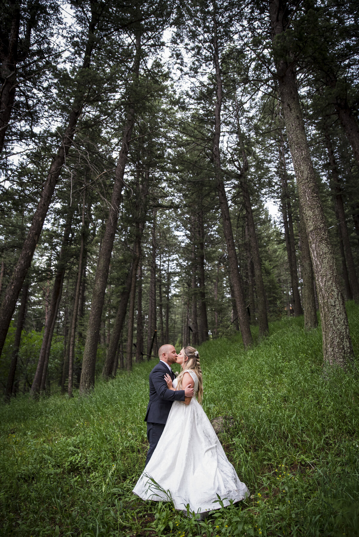 A wide angle shot of a bride and groom sharing a kiss among the pine trees at The Pines at Genesee..