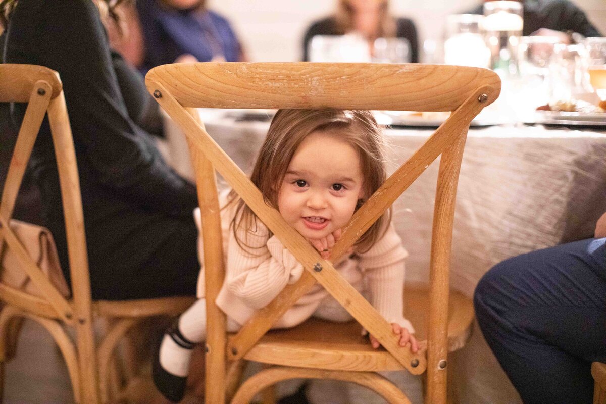 cute little girl plays peek a boo with chair at wedding reception
