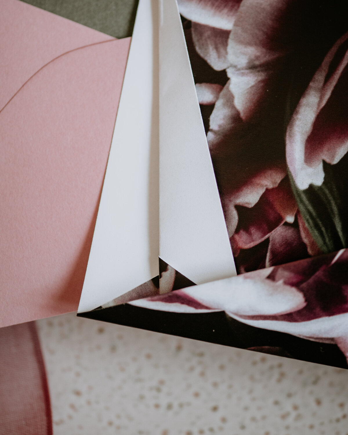 Corner of folded origami wedding invitation with dark pink flowers