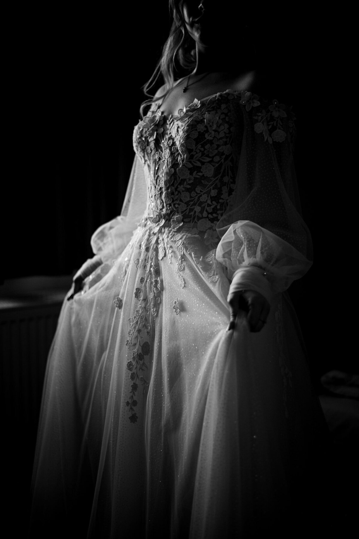 schwarz weiß Foto der Braut, die die Stickereien ihres Brautkleids zeigt