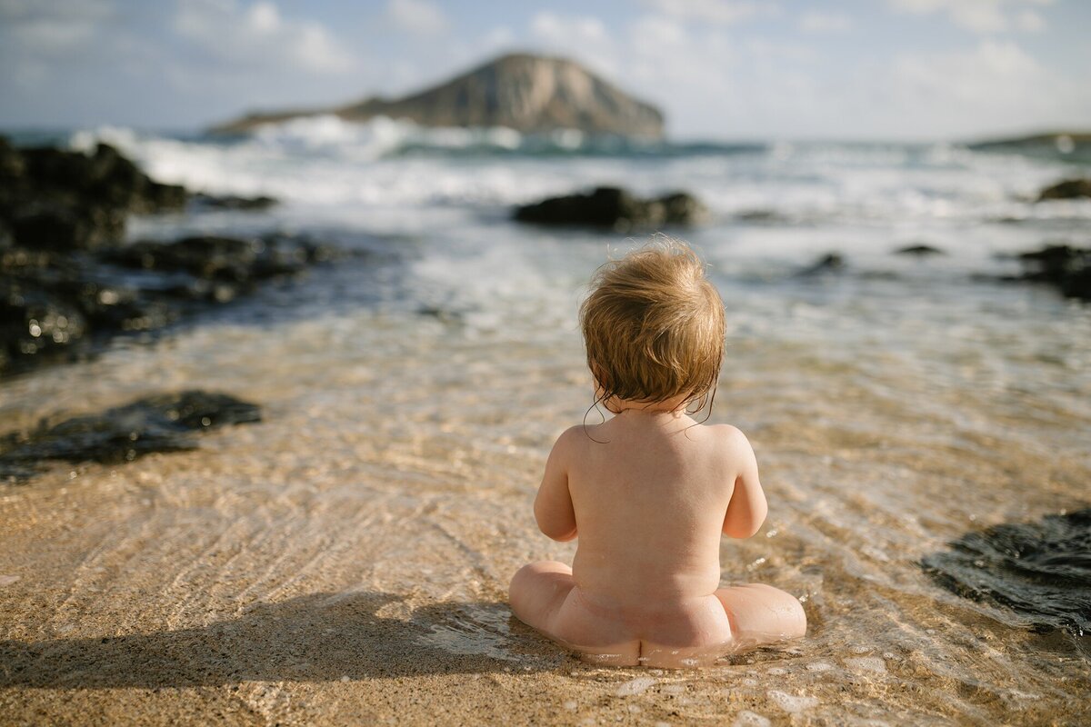 naked baby sitting in shallow water at makapuu beach oahu