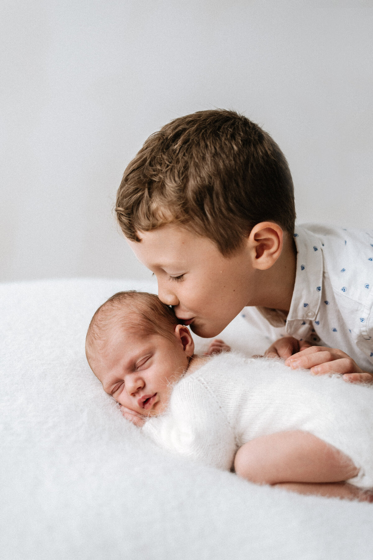 Big brother kissing newborn sisters head at a newborn photoshoot in Billingshurst