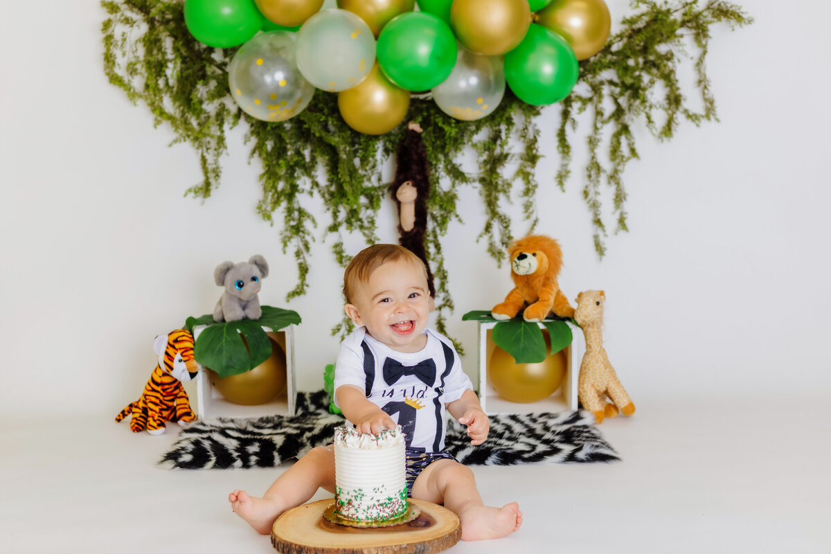 Cake Smash Photographer, a baby has hands in cake at jungle themed party