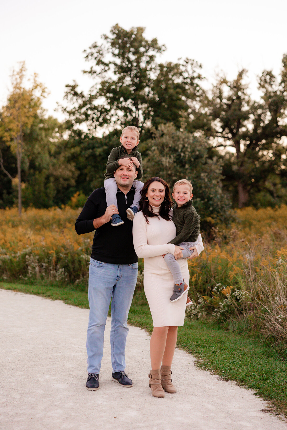 Dad puts one son on his shoulders and moms hold the other son on her hip for a family portrait