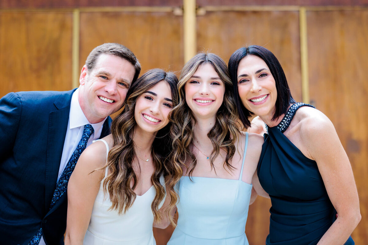 A mom, dad and two sisters smile together in dresses and a suit in front of a temple
