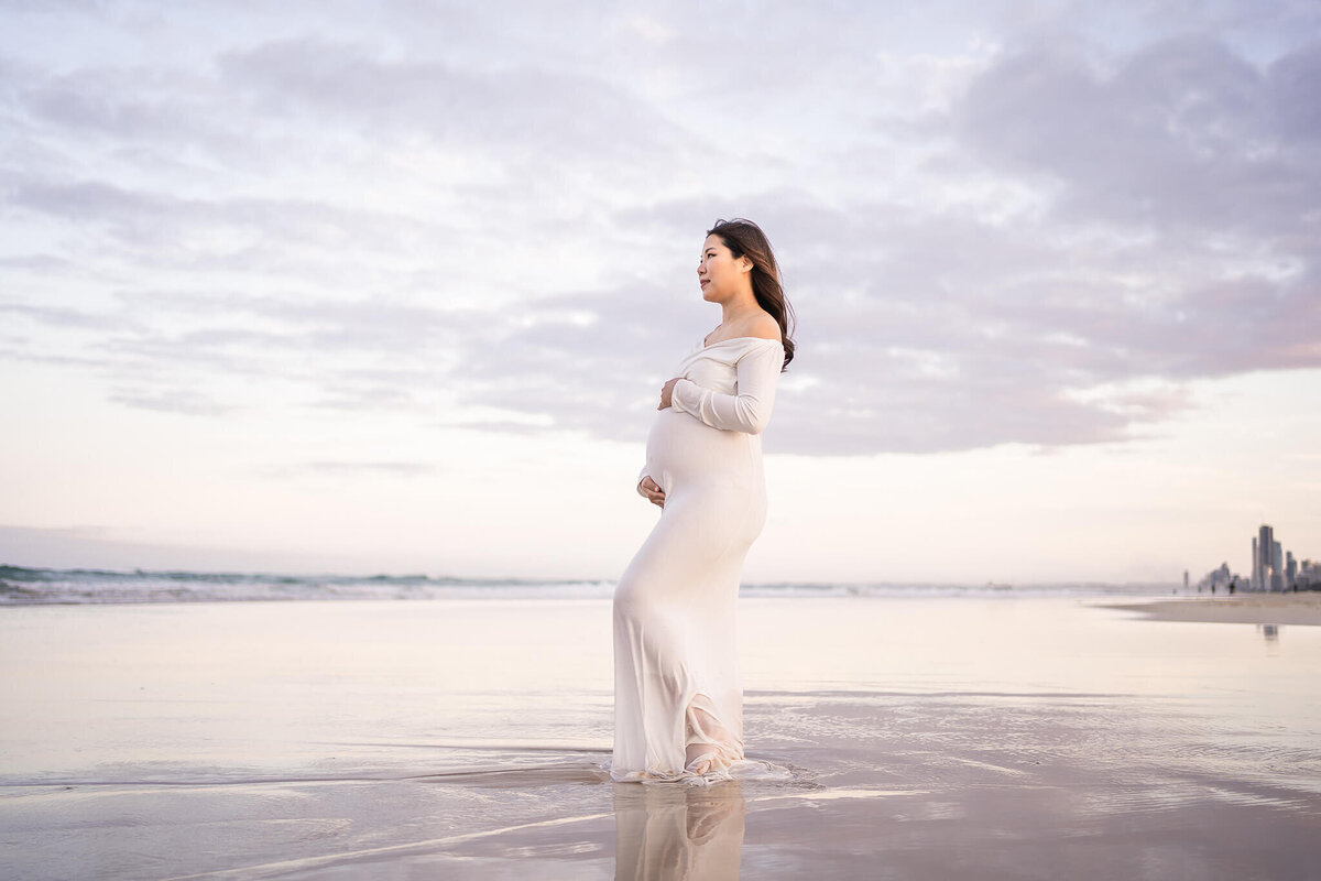 Elegant woman in white dress in water having maternity photography done in Gold Coast