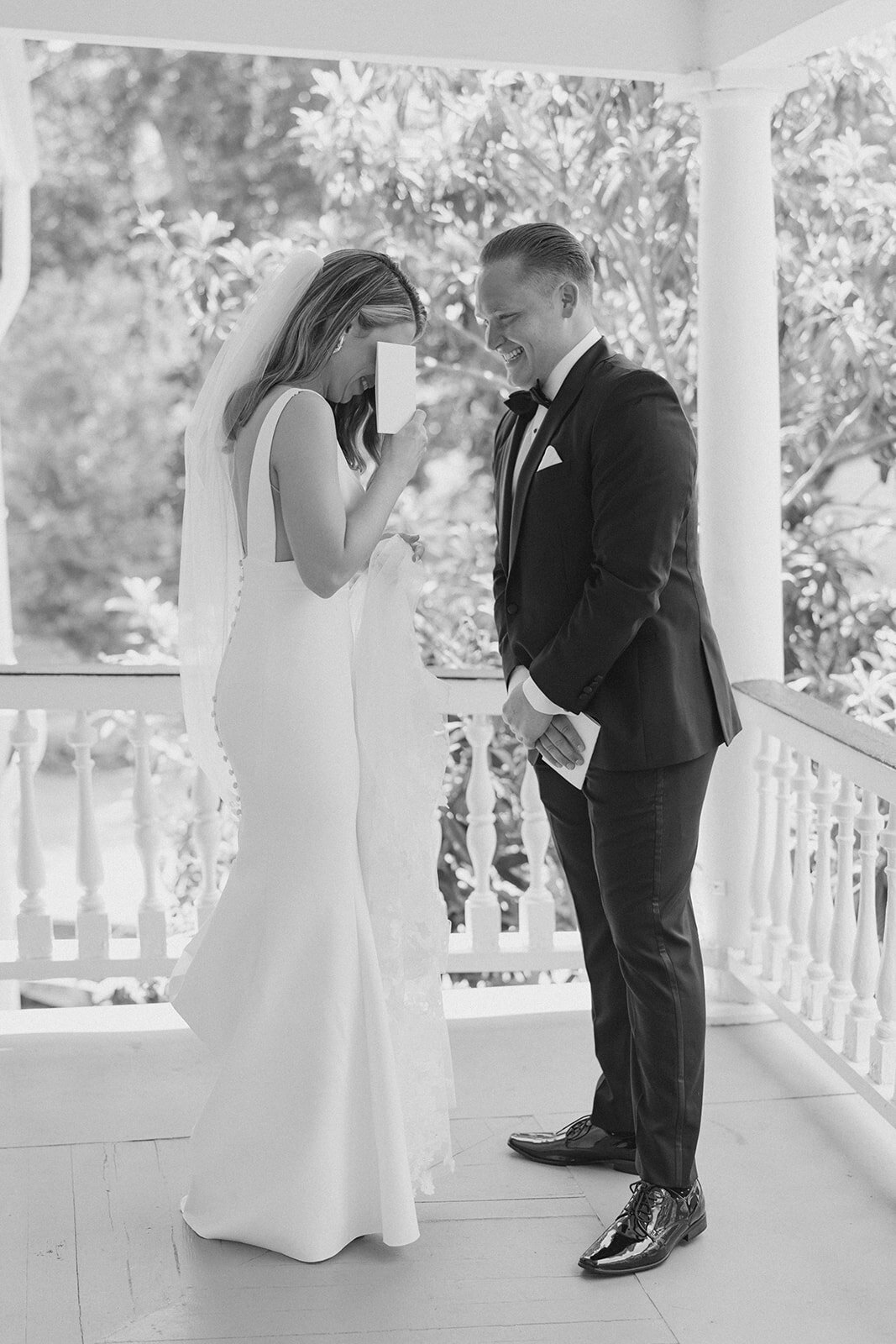 Private vow reading on a porch in downtown Charleston. Bride covers her eyes with groom smiling at her during cute candid moment on wedding day. Charleston wedding photographer.