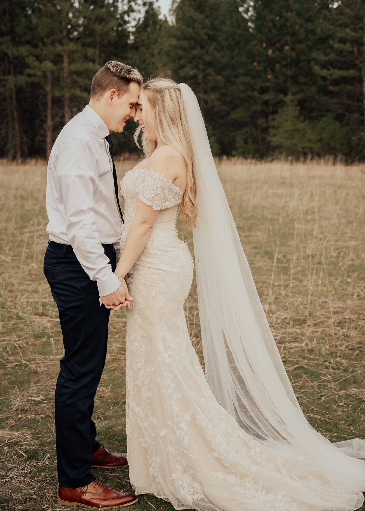 Maddie Rae Photography bride and groom standing face to face holding hands. they are touching foreheads and smiling at eachother. her dress and veil are flowing down behind her