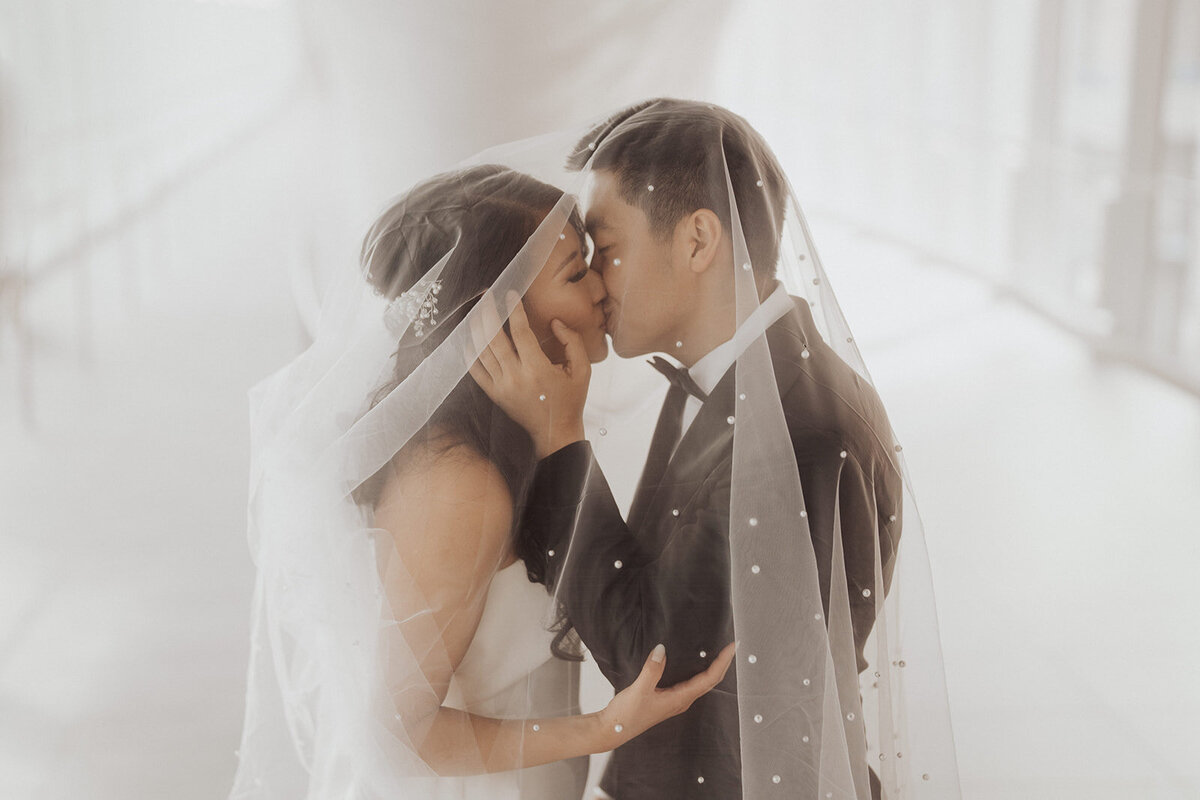 A veiled couple sharing a kiss in a soft-focus setting.
