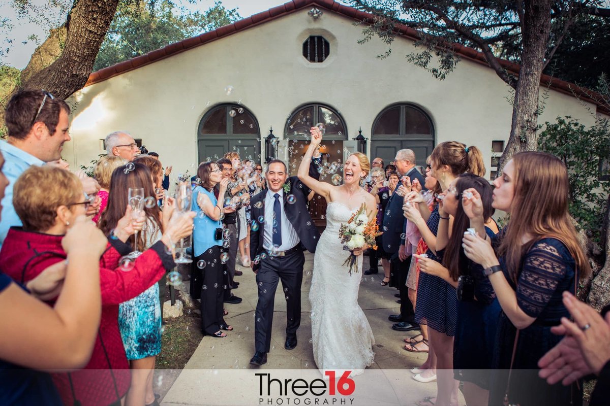 Bride and Groom walk down the aisle with arms in the air to celebrate as the wedding guests applaud