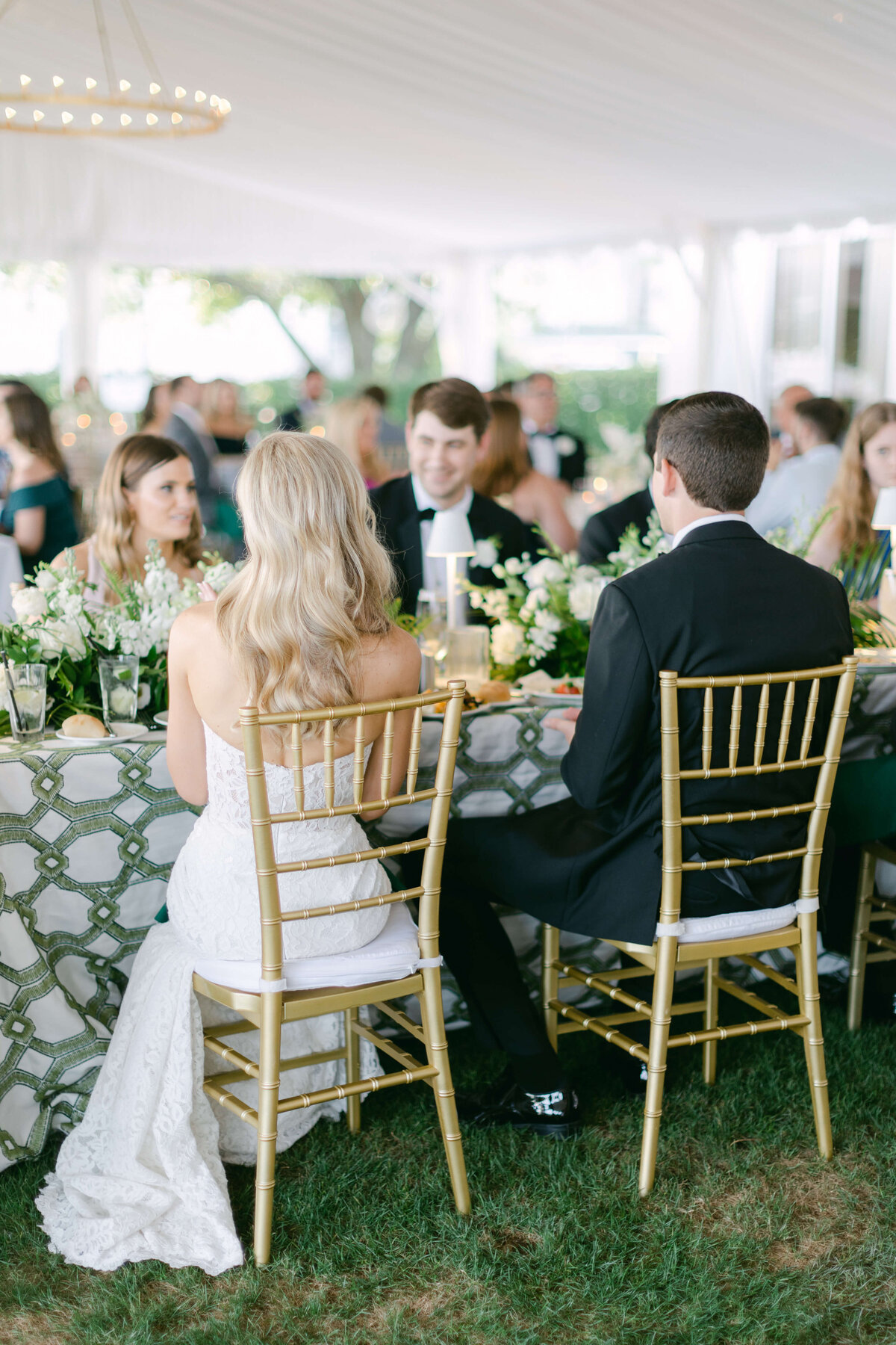 A bride and groom sit in chairs at their wedding reception.