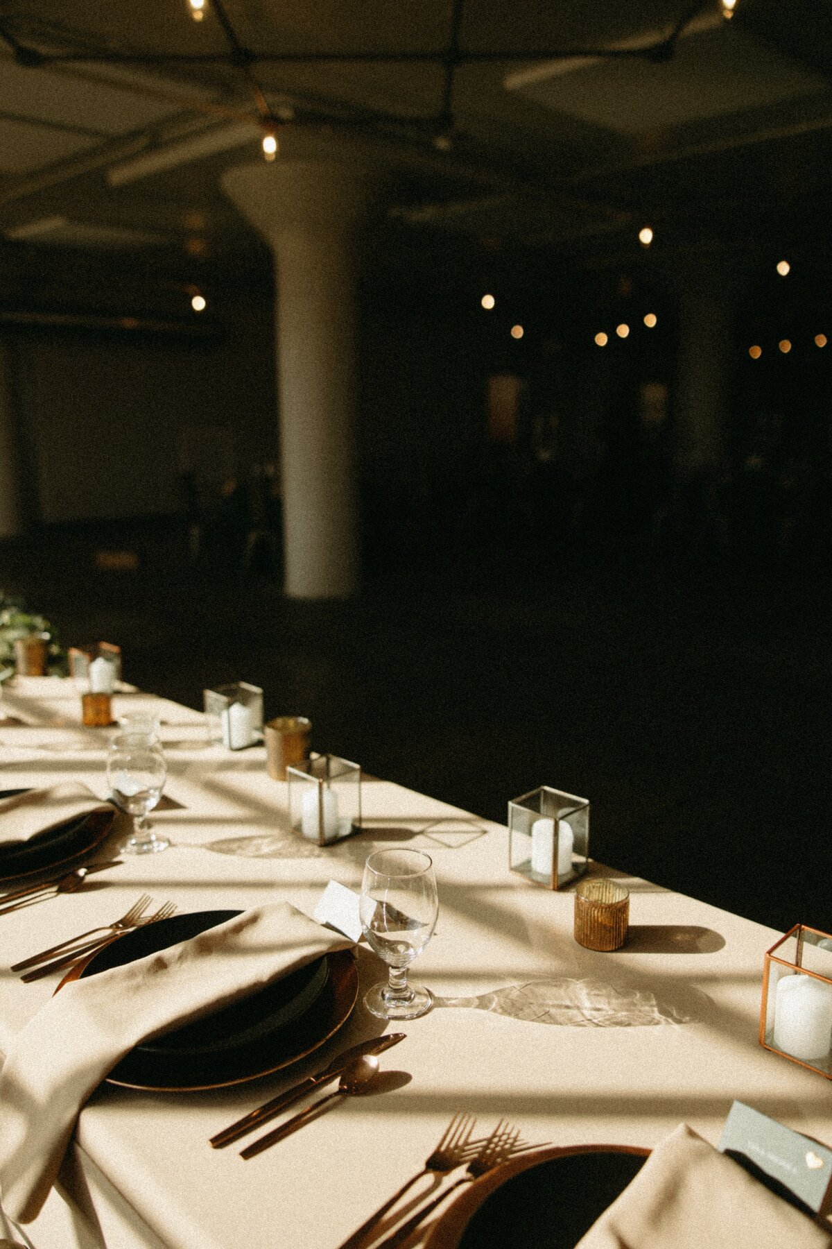 Elegant dinner setup in a dimly lit room with a long table covered in a white cloth, featuring plates, silverware, and small decorative items, perfect for events in Davenport.