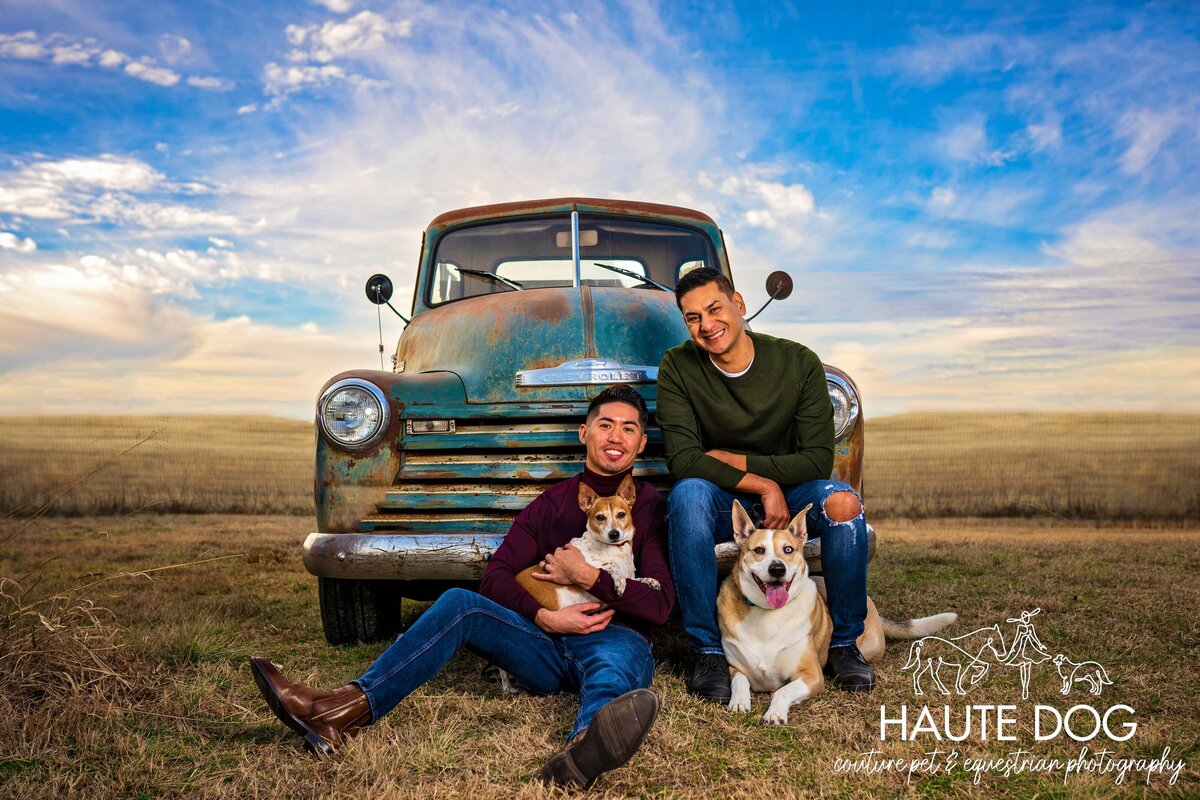 LGBTQ+ couple sit in front of a vintage truck with their two dogs.