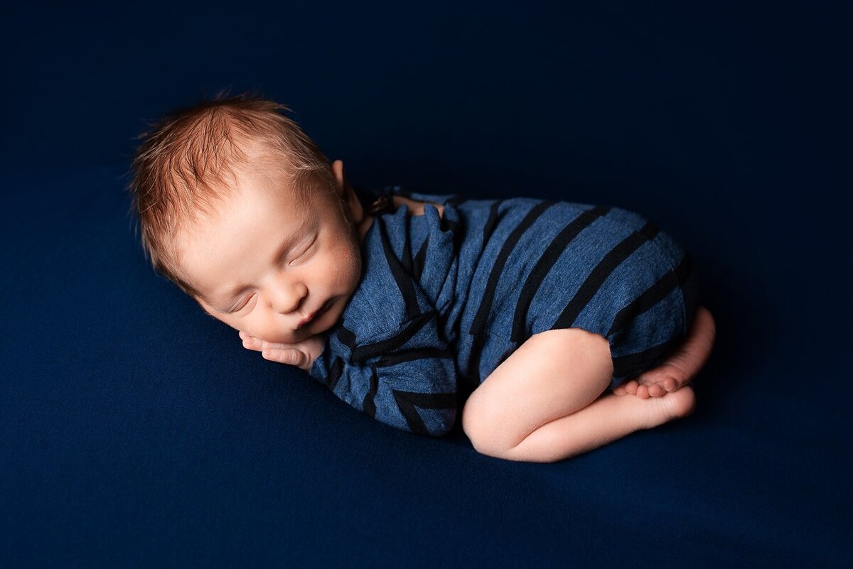 Newborn baby boy in bum-up pose wearing blue striped romper