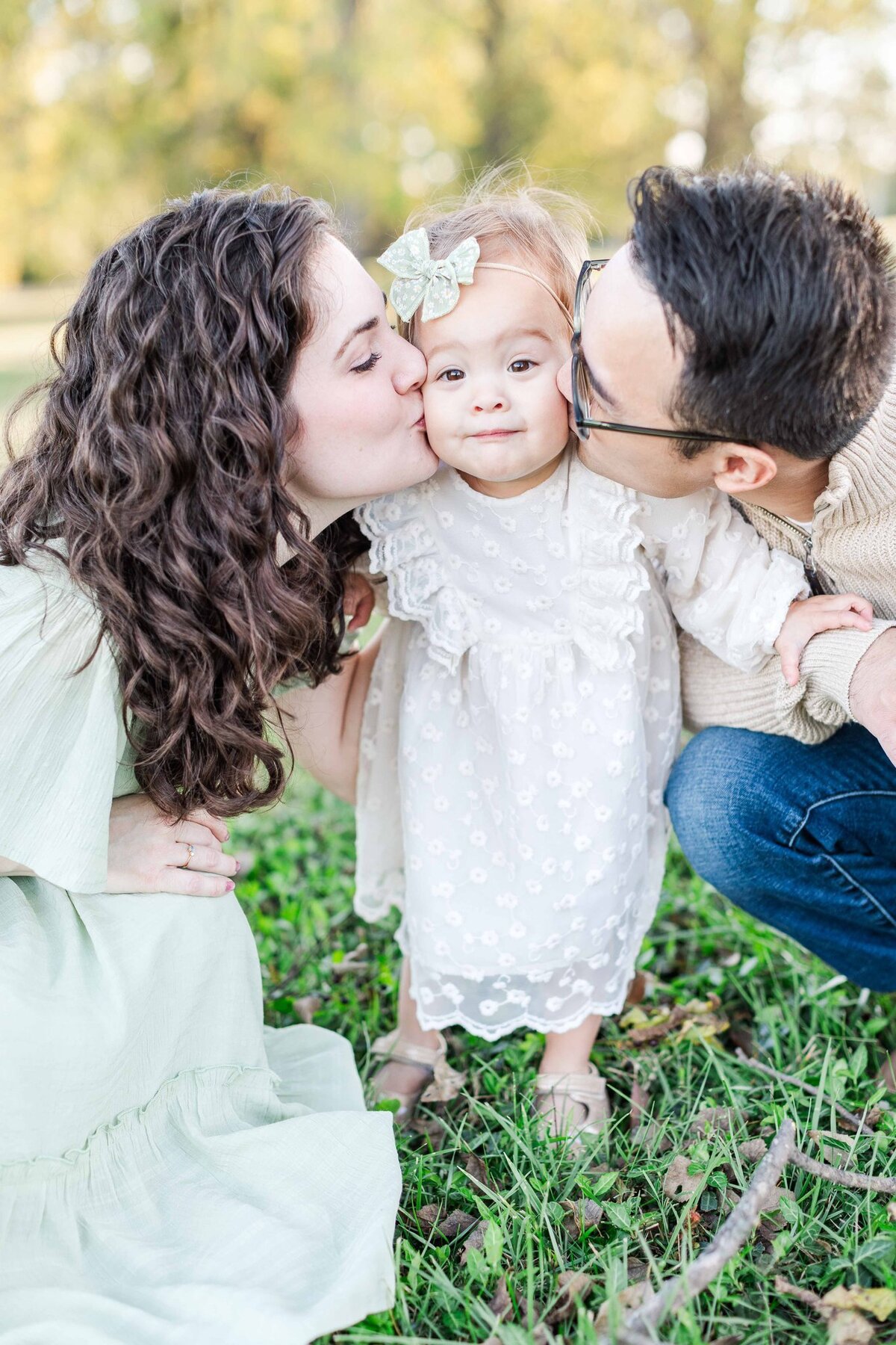 Mother and father kissing baby girl in a field during spring in Tennessee