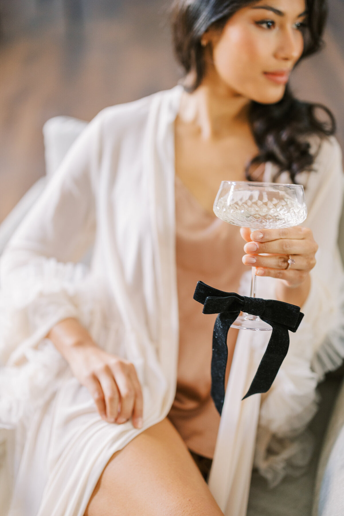 A woman poses in a luxurious robe with a glass of champagne for a boudoir photo