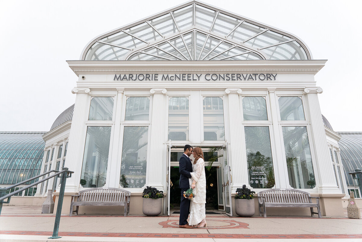 Bride and groom kiss in front of Como Zoo Conservatory.