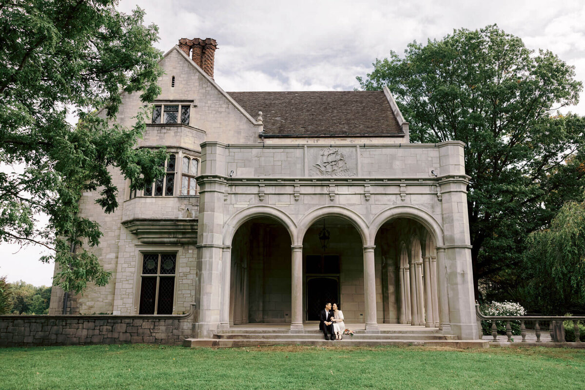 The engaged couple is sitting in the entrance staircase of Coe Hall at Planting Fields Arboretum, NY. Image by Jenny Fu Studio
