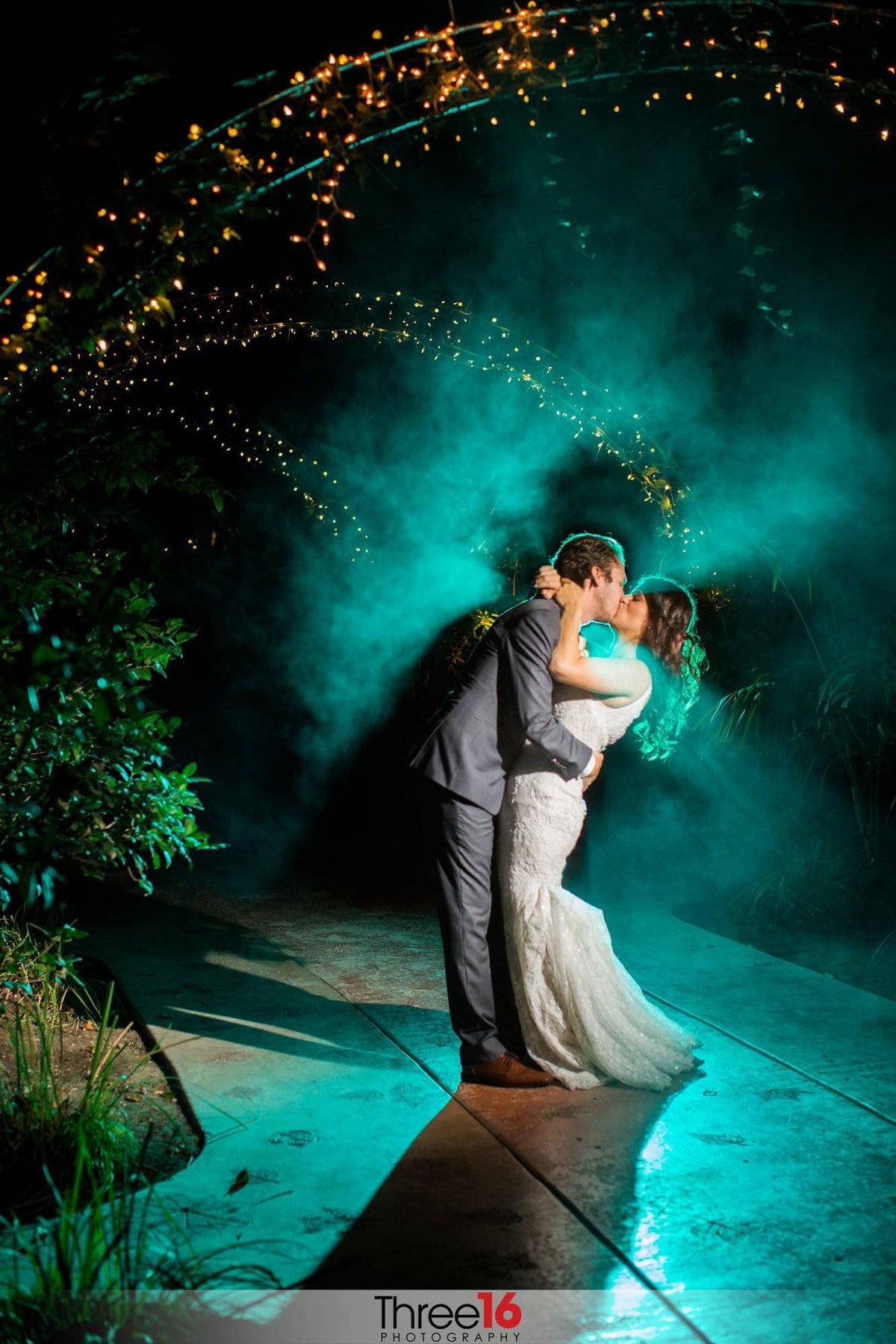 Bride and Groom share a romantic night kiss under the gazebo with green mist behind them