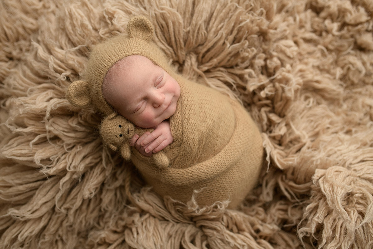 Newborn boy smiling holding teddy bear during boston newborn session