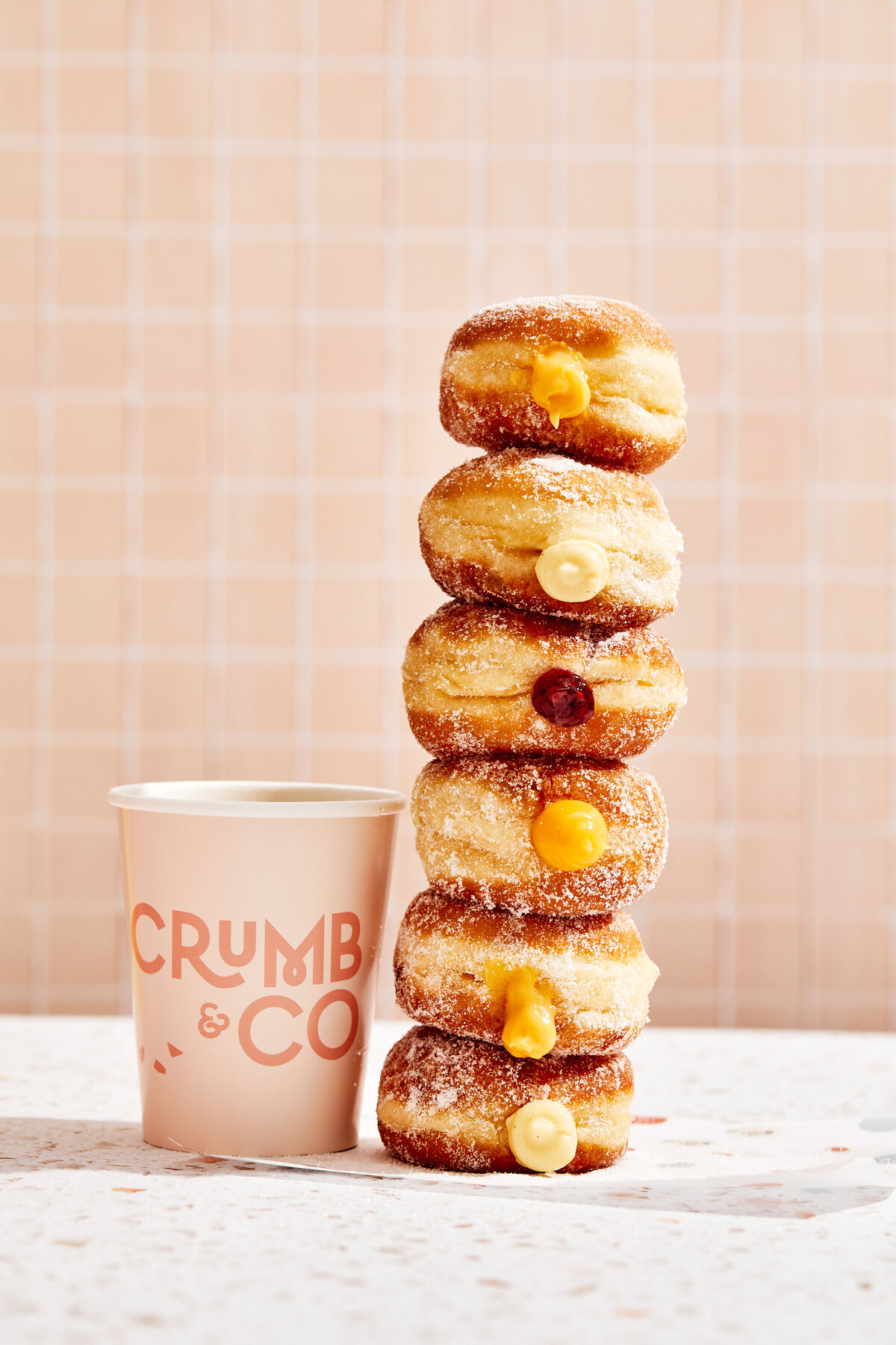 A cup of fresh coffee and a tall stack of filled sugar jam and cream  donuts.