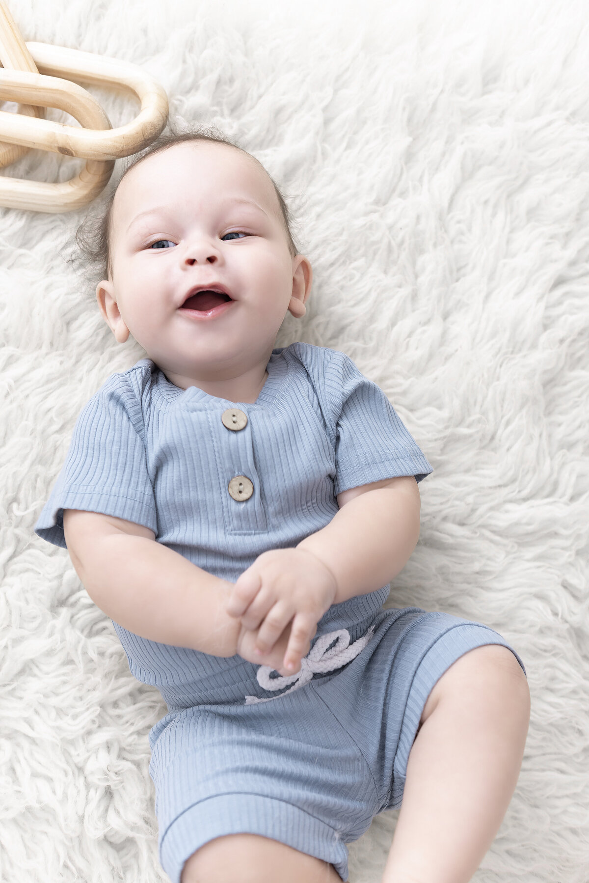 A happy young baby lays on a shag blanket smiling in a blue onesie