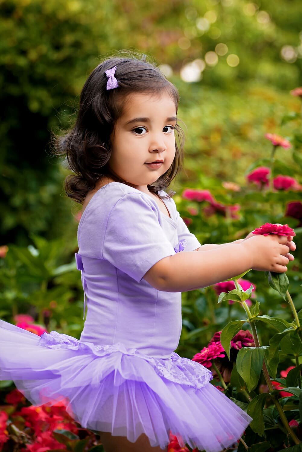 Outdoor child portrait of 2 year old girl in purple tutu playing in flowers at Deer Lake Park