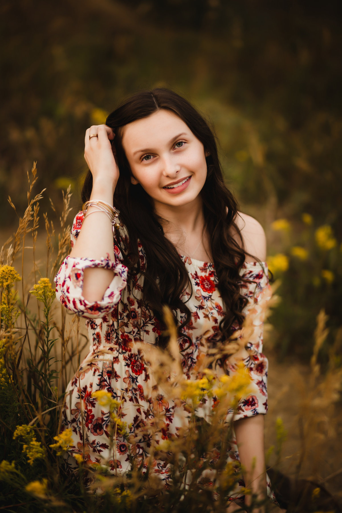 girl holds hair in front of yellow fall flowers for senior photos in thornton colorado