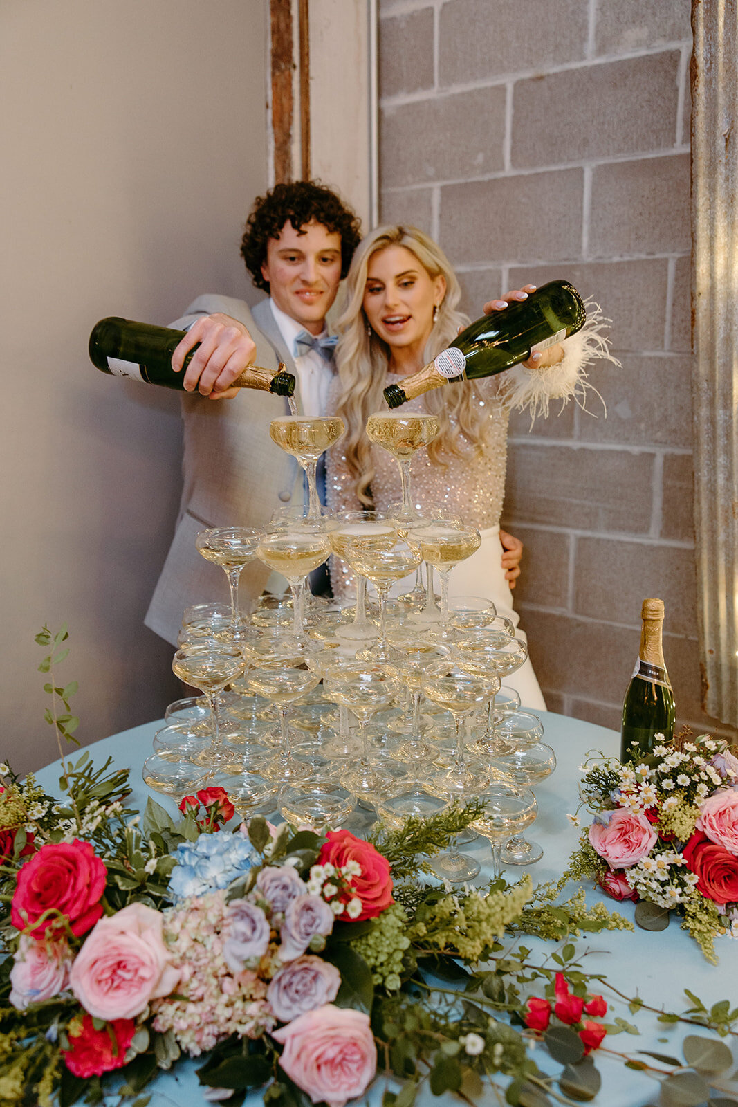 Bride and Groom pouring champagne on a champagne tower  surrounded by flowers