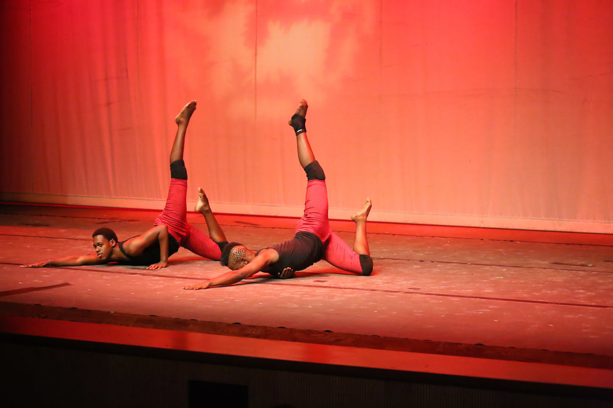 Two male dancers dressed in red and black perform on theatre stage. Photo by Ross Photography, Trinidad, W.I..