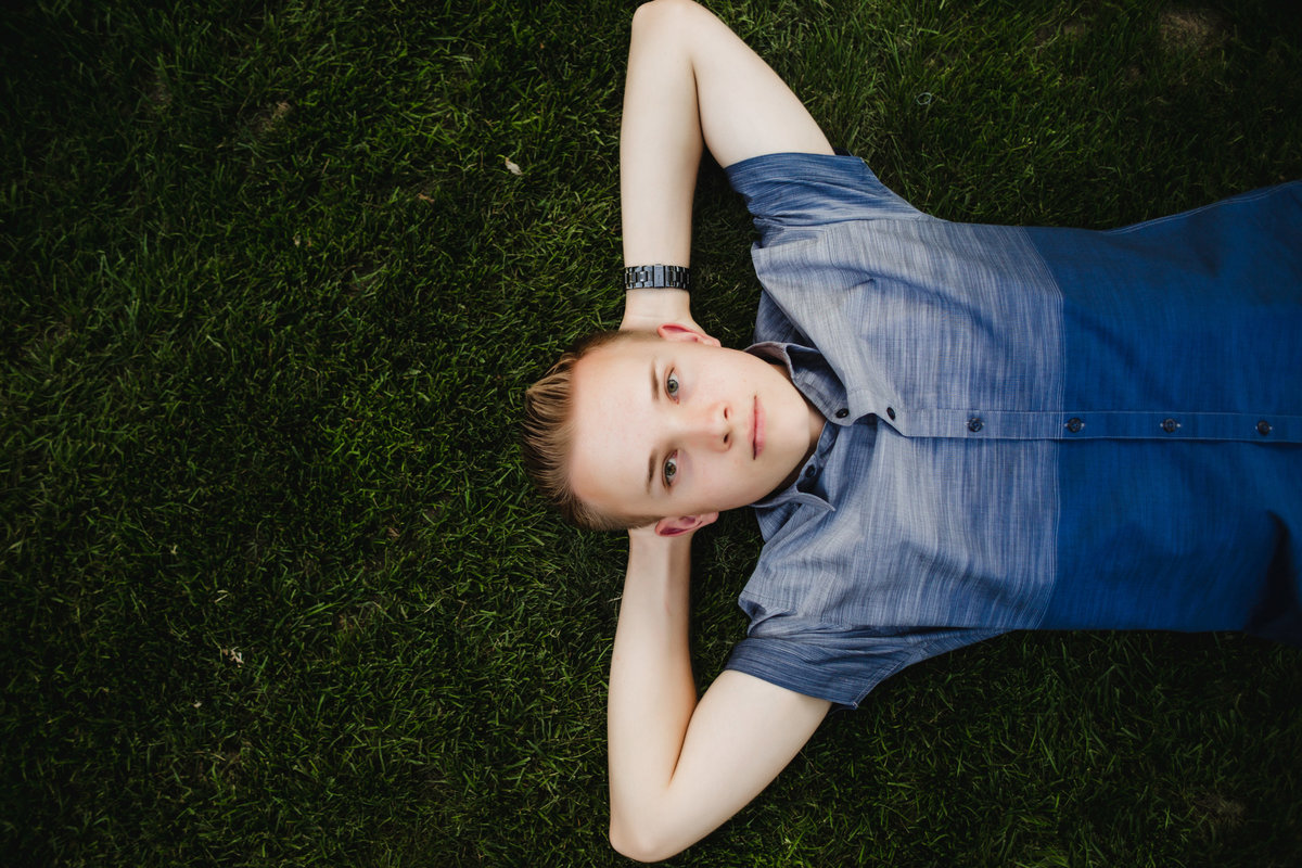 teenage boy lays on his back in grass for senior photos in thornton colorado