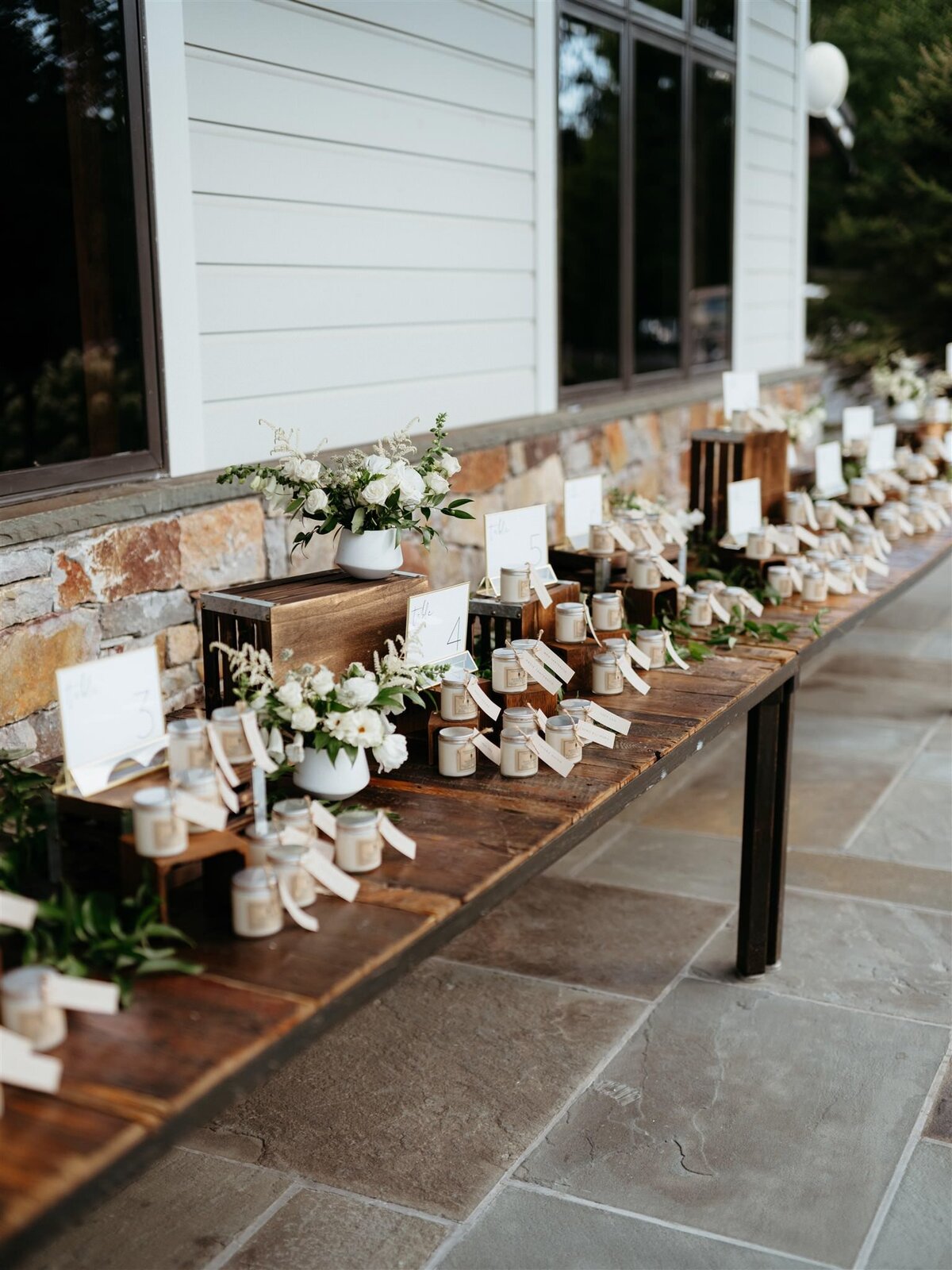 Timeless display of wedding favors, white and green bouquets on deep brown farmhouse table at Cedar Lakes Estate in Hudson Valley.
