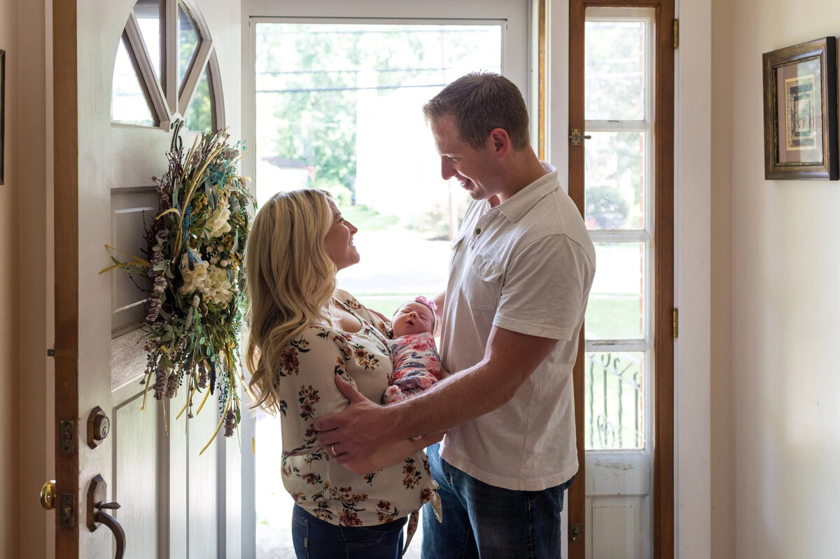 Mother and father, looking at each other, while holding their newborn baby in front of the door