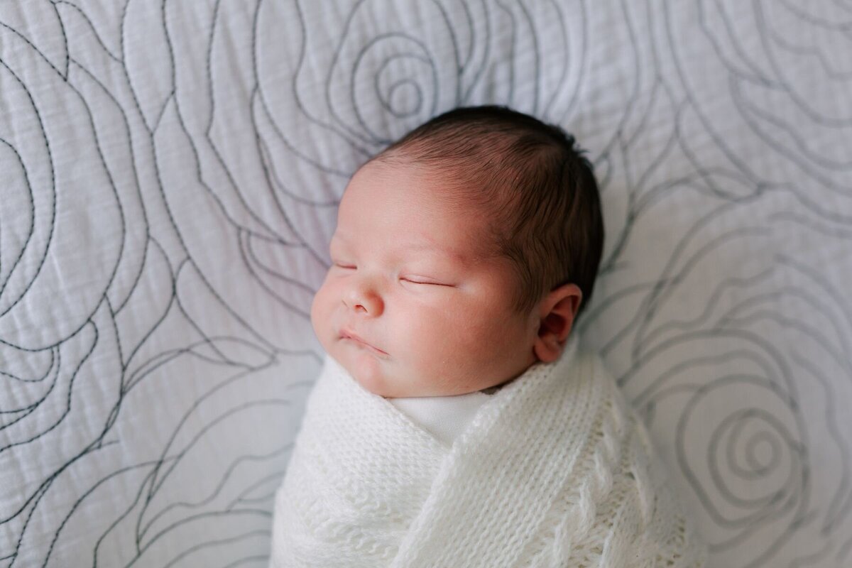 Newborn baby boy is sleeping while swaddled for his newborn photography session .