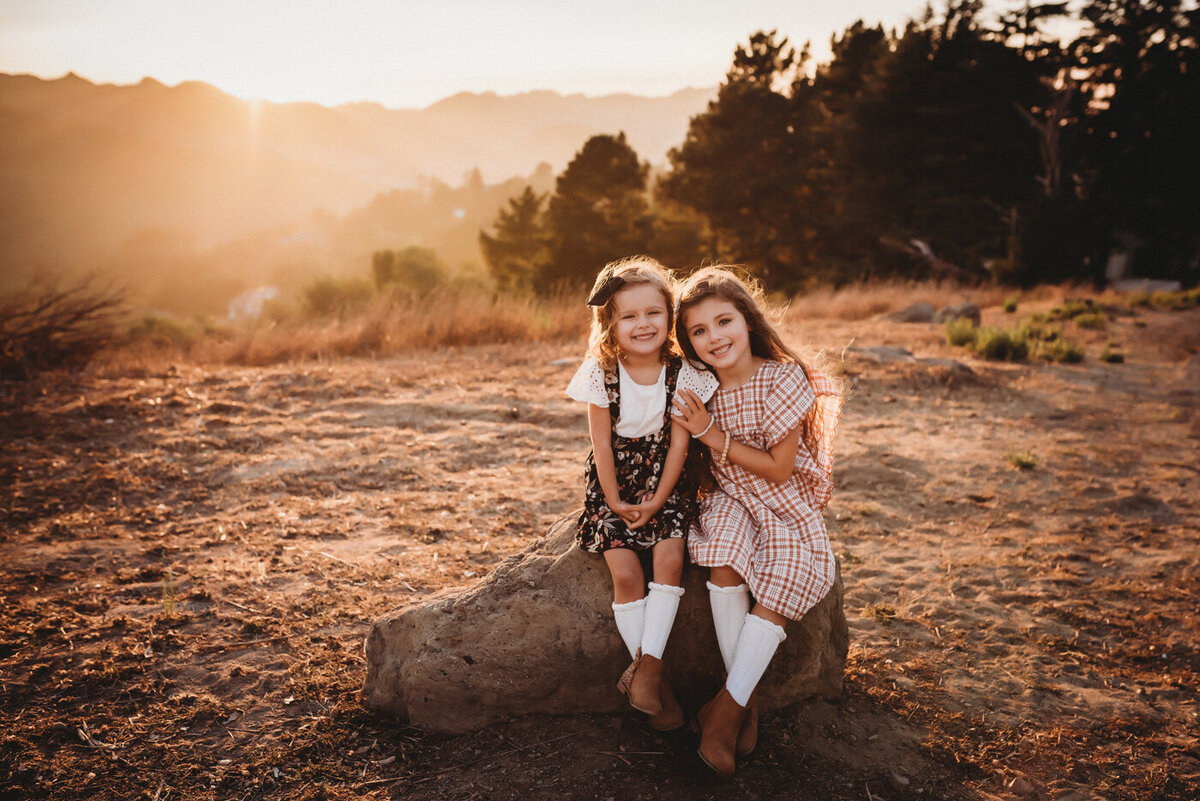 Sweet sisters smiling at the camera while sitting on a rock in the East Bay hills