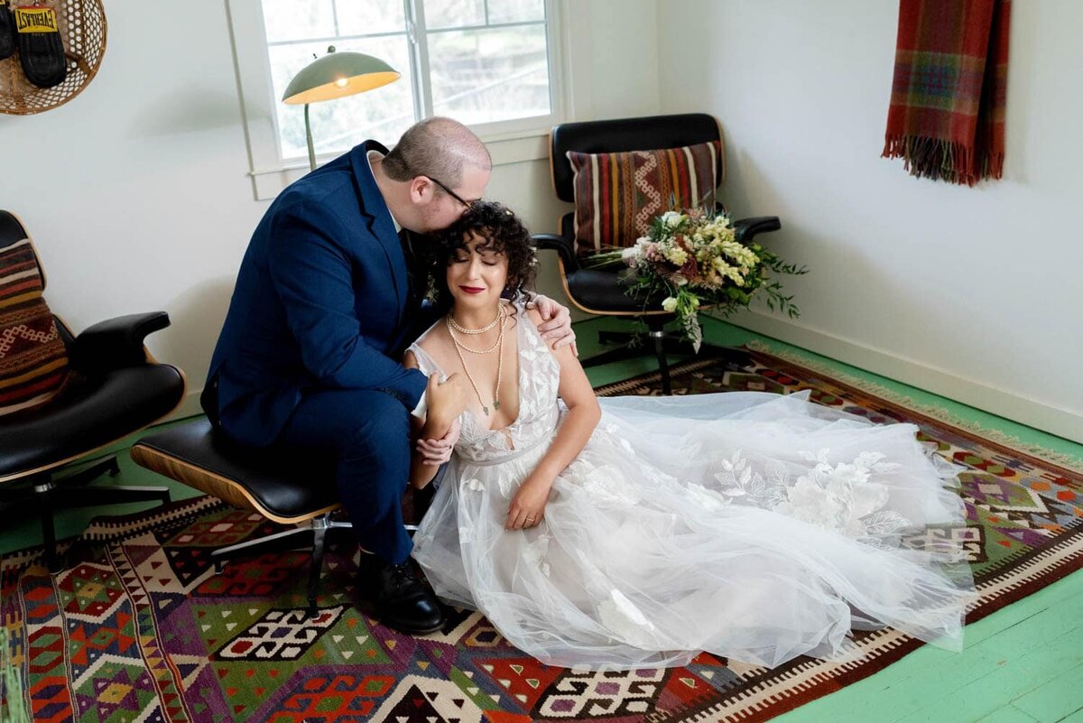 a bride and groom sit on a colorful run and a green hardwood floor and kiss at lodge 902 in hood river