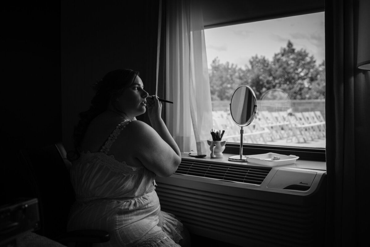 the bride using the window light to put on makeup