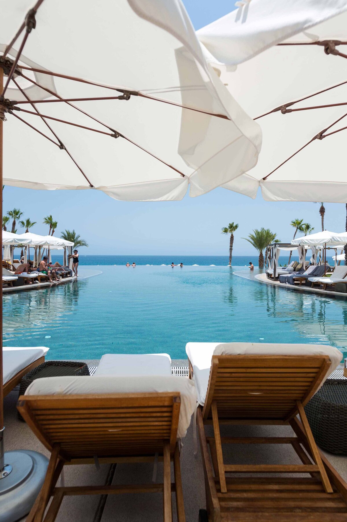 Two teak lounge chair with white umbrellas and vanishing edge pool at the Hilton Los Cabos