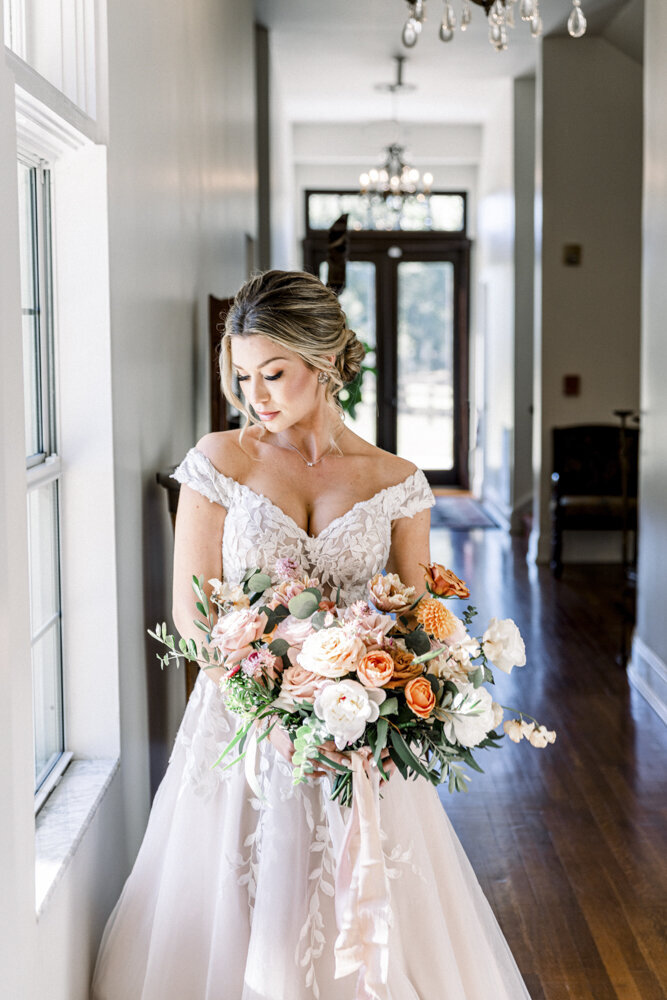 bride holding a bouquet and standing next to a window