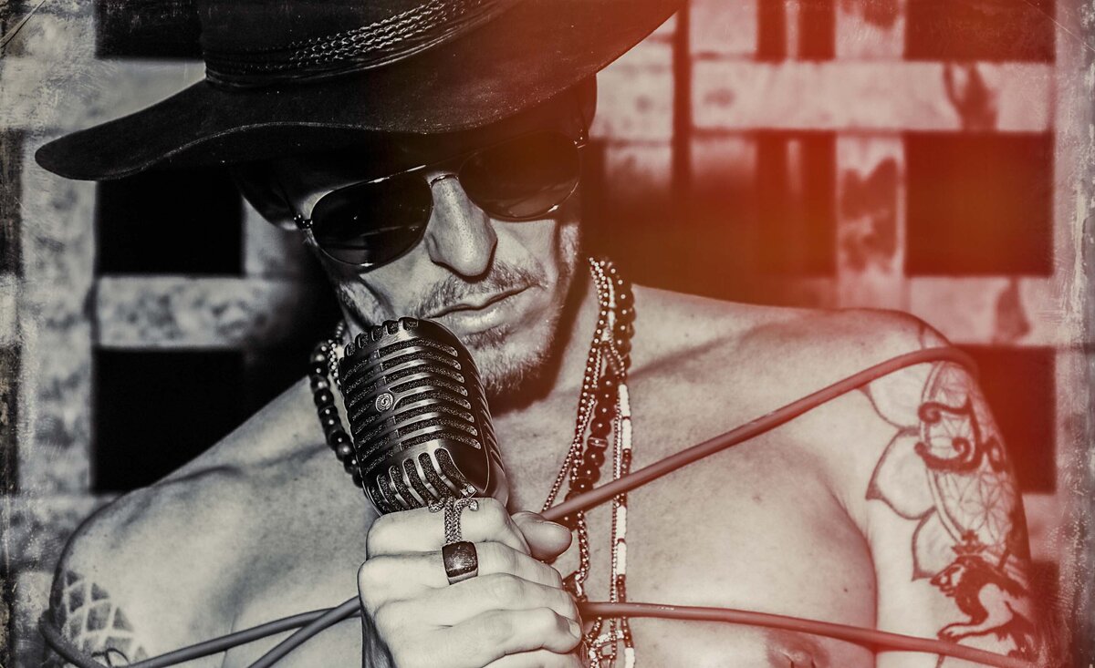 Male musician portrait CJ Shaman holding vintage mic wearing cowboy hat sunglasses black and white