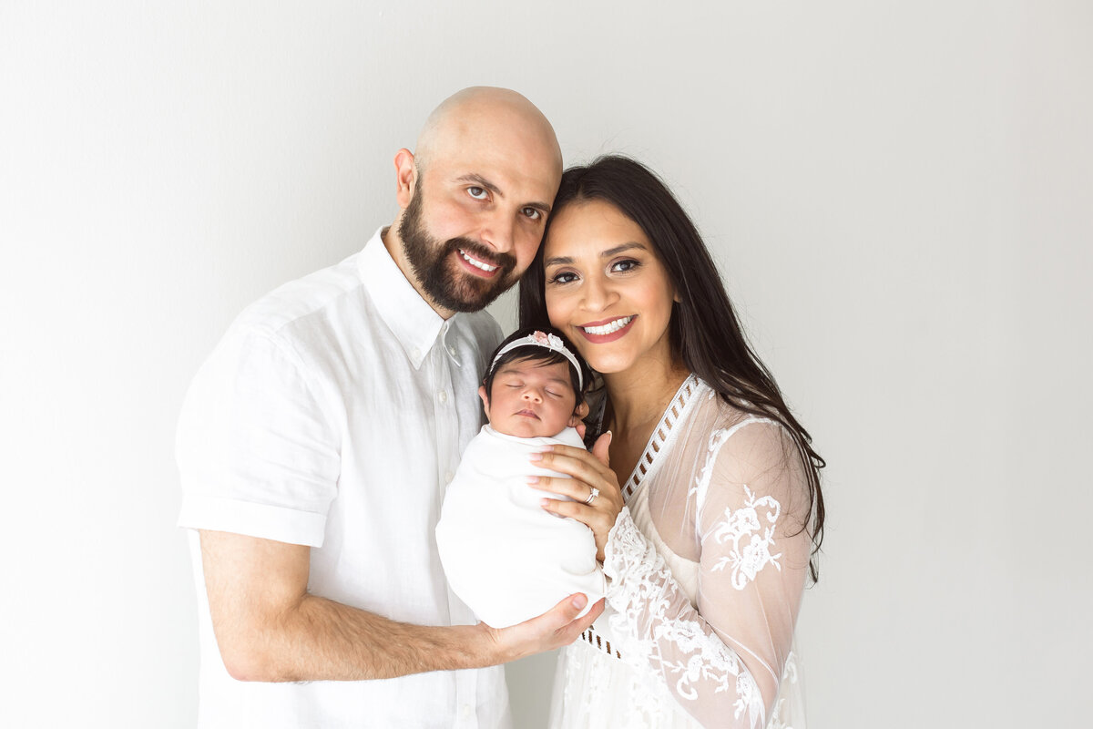 two parents smiling looking at camera and holding newborn baby