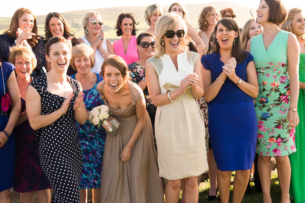 Many female wedding guests in colourful outfits laughing together with bridesmaid with taupe bridesmaid dress